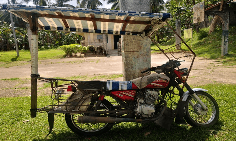 A red habal-habal motorcycle in Mahaplag fitted with an extended passenger frame and a large roof.