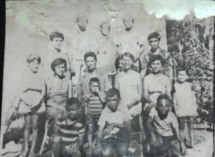 A faded black-and-white outdoor group portrait of children and adults.