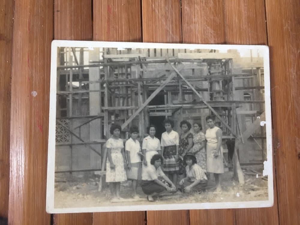A photographed print showing nine women posed in front of a building under construction.