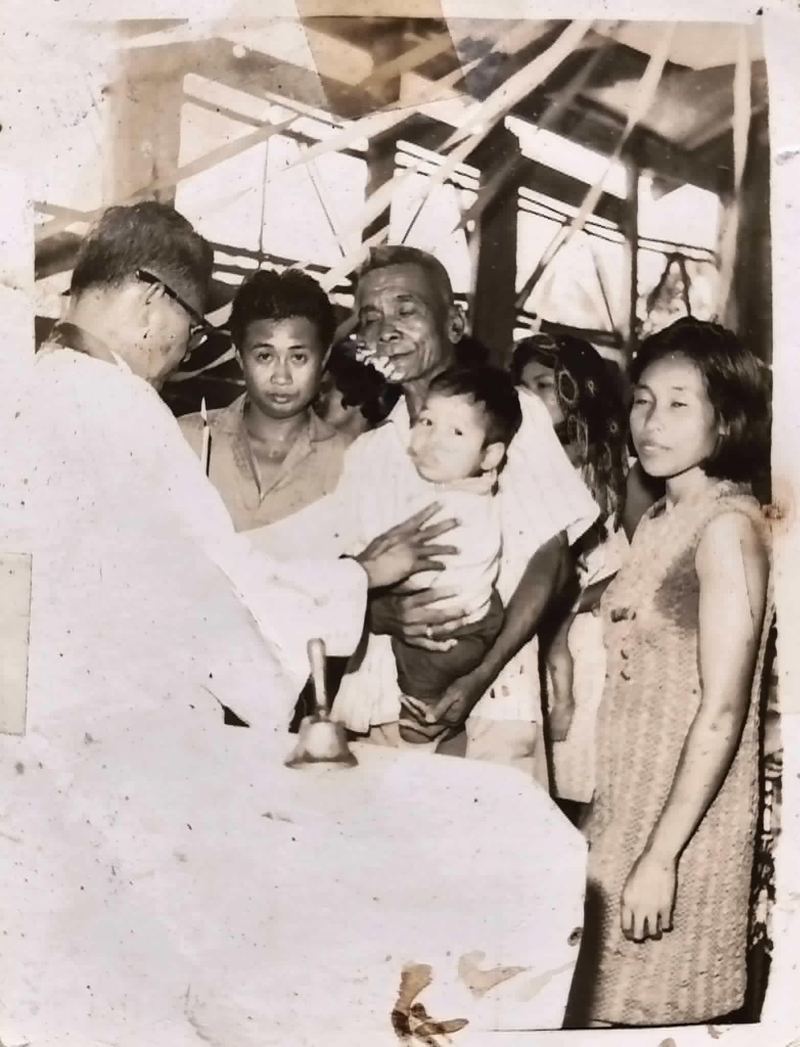 A priest conducts a religious rite for an infant held by an adult as family members look on.
