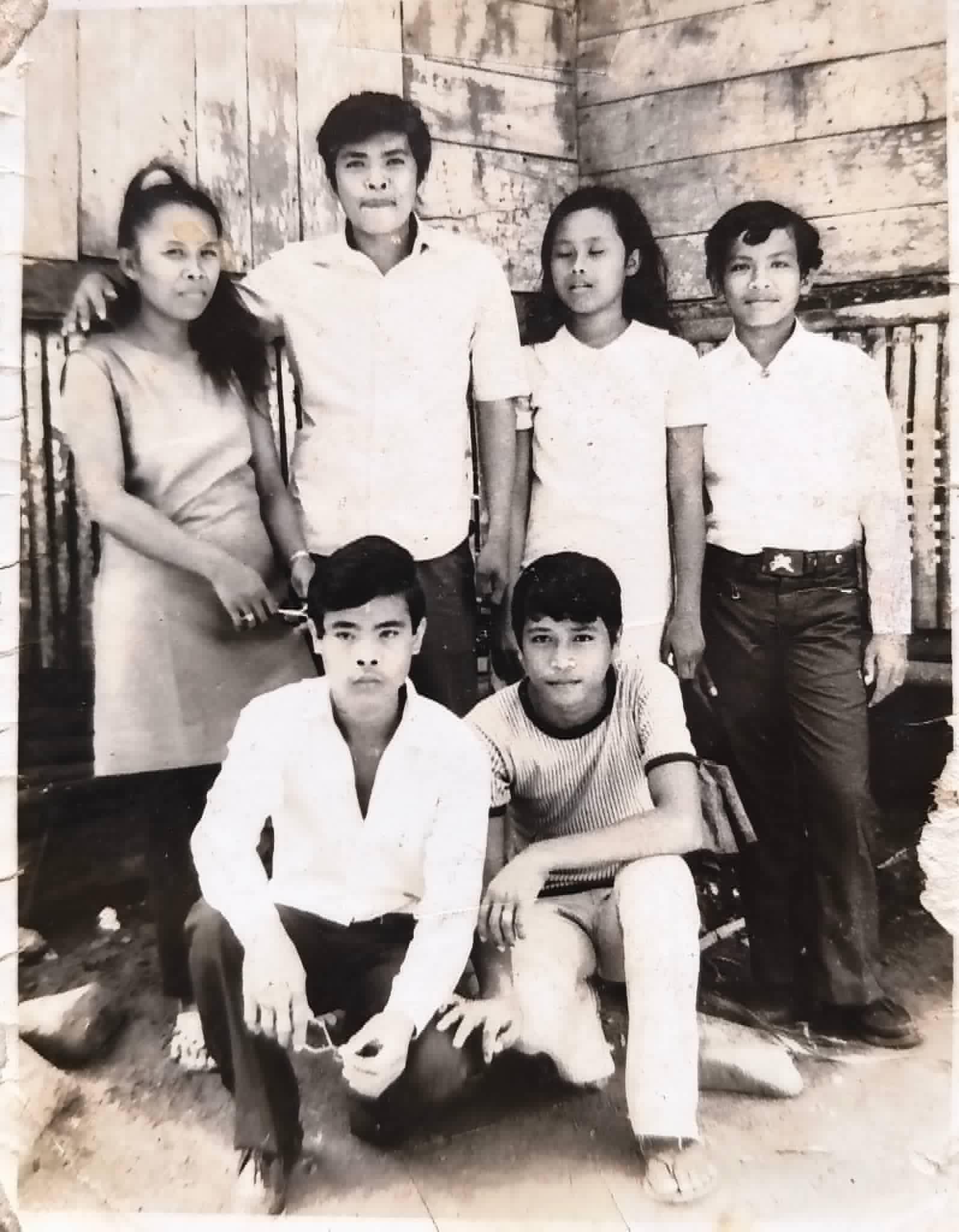 Six young adults pose together in front of a wooden building.
