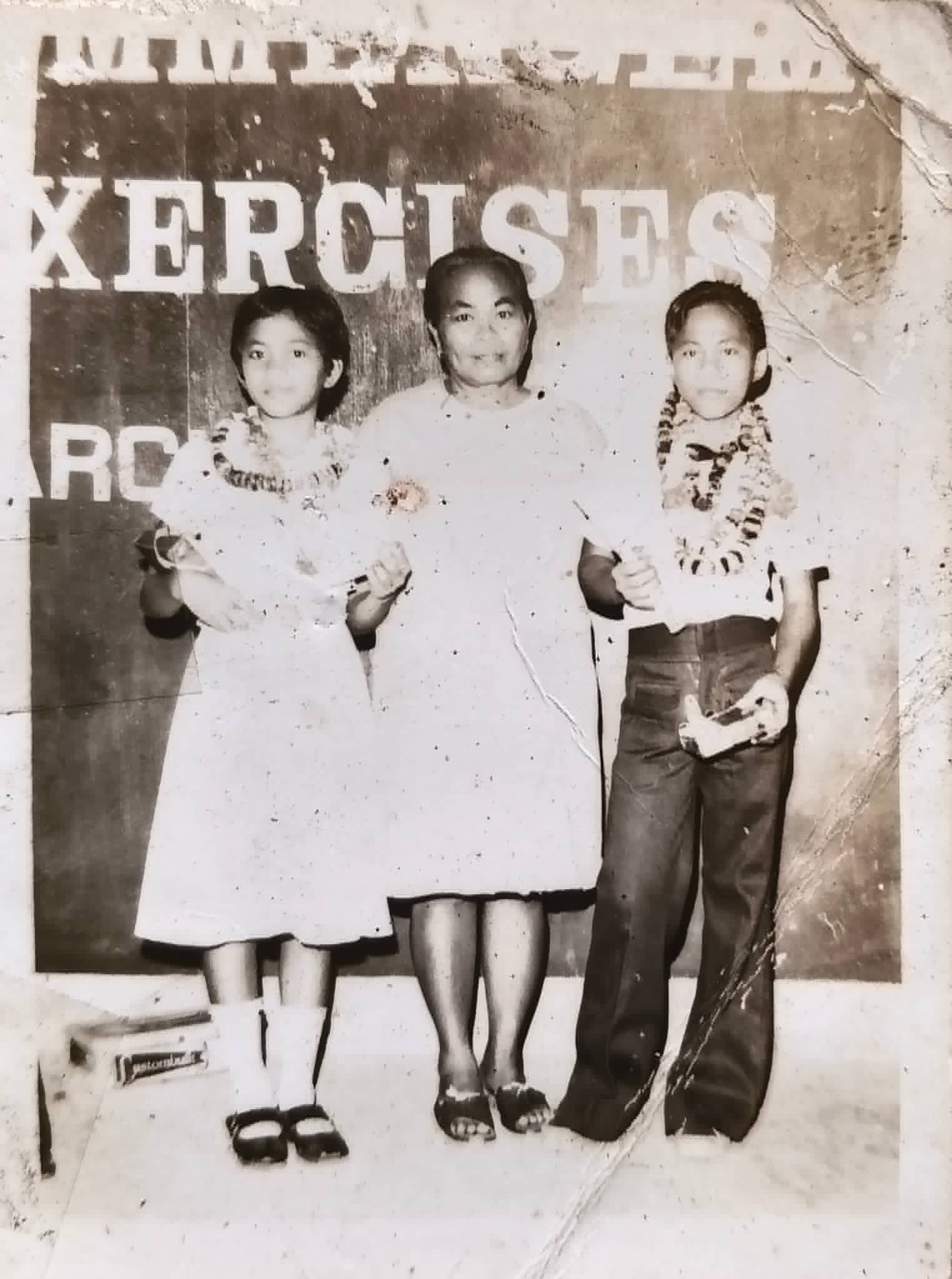 Three people wearing garlands stand before a backdrop with the word Exercises.