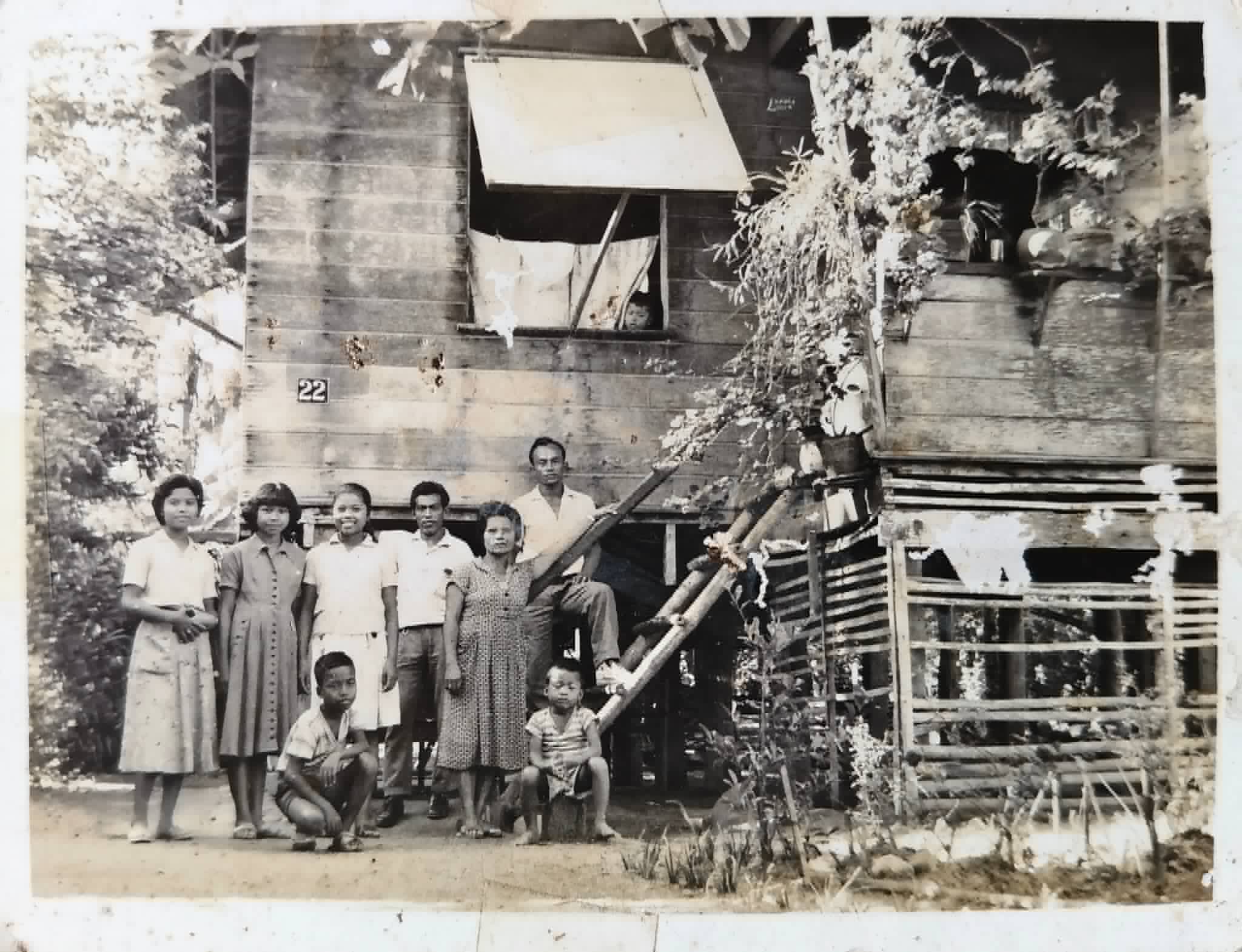 A family group poses in front of a raised wooden house marked with the number 22.
