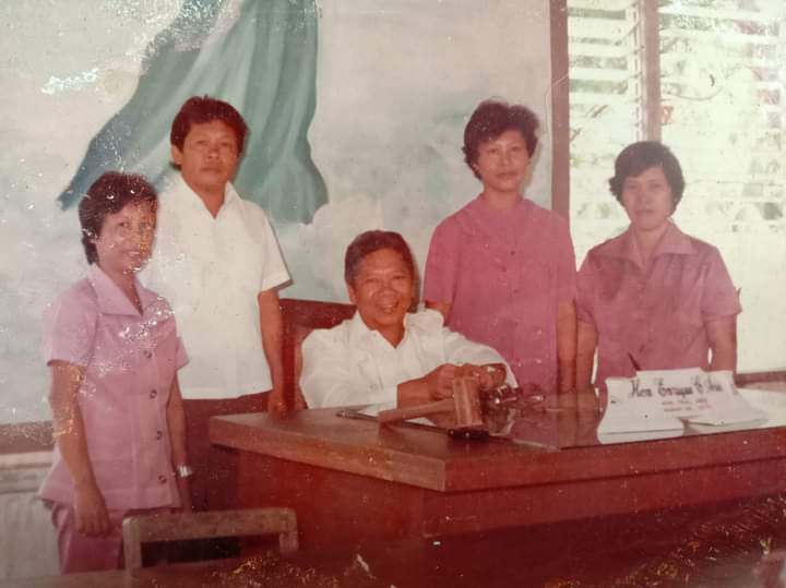 Five adults pose around an office desk, with one person seated behind it.