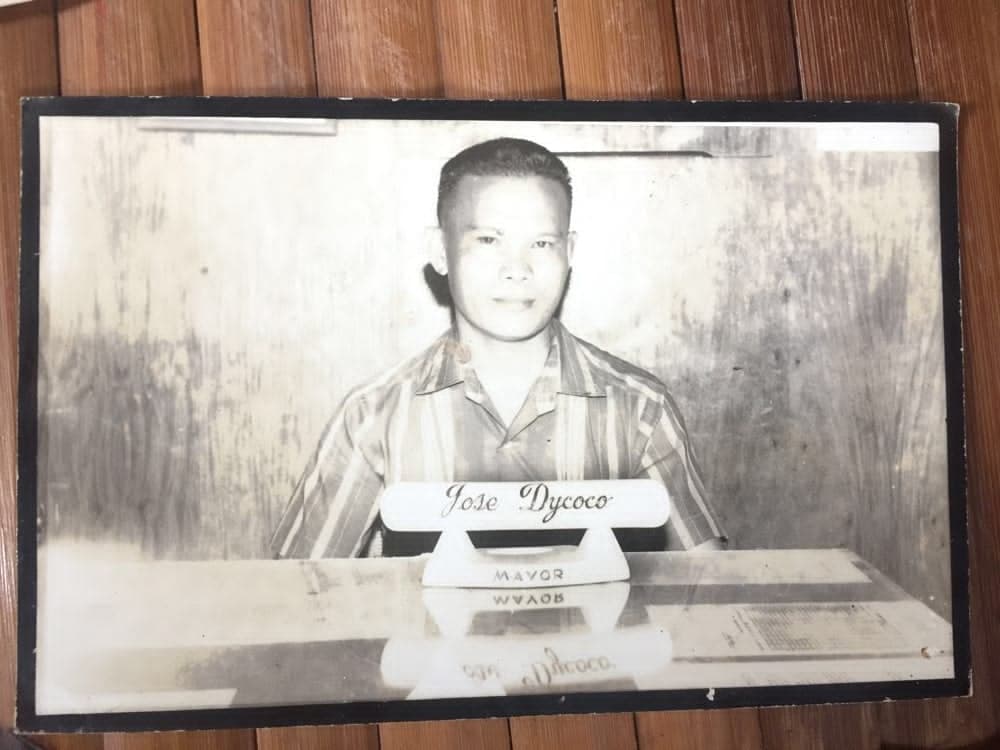 Jose Dycoco sits behind a desk with a nameplate identifying him as mayor.